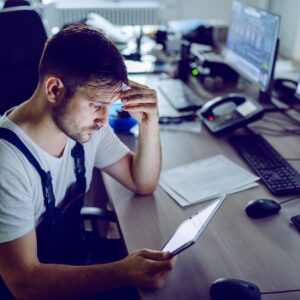 Serious caucasian plant worker using tablet while sitting in control room.